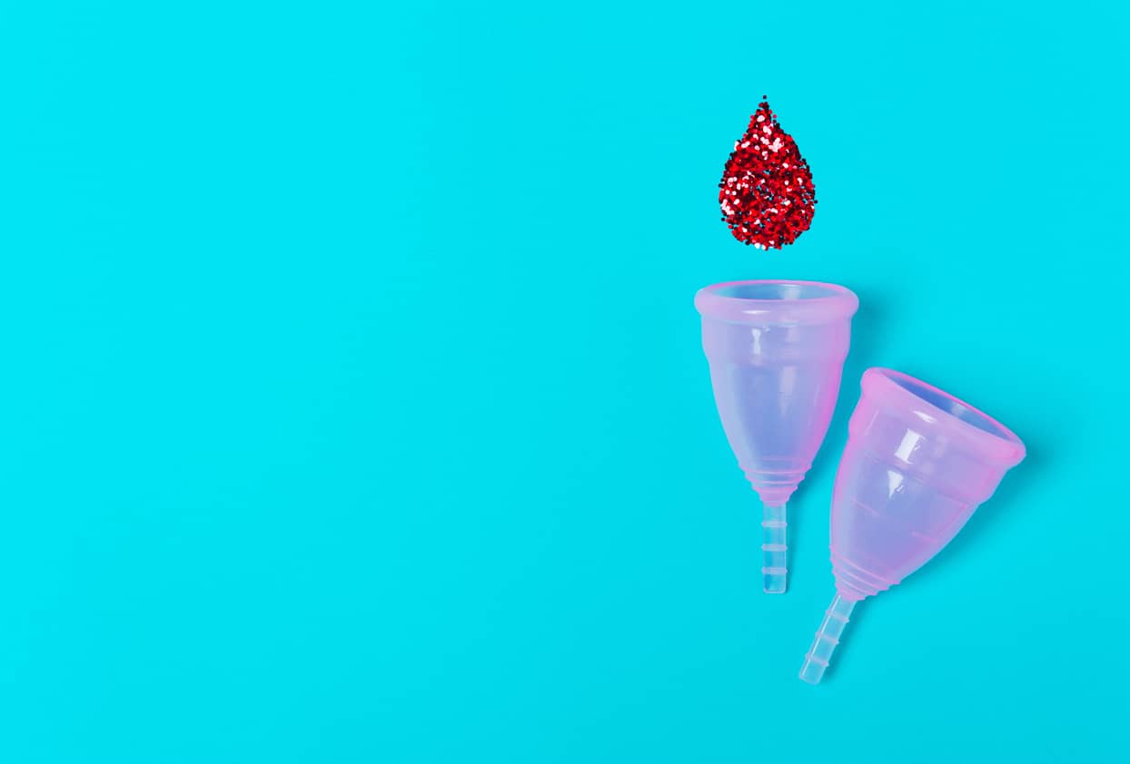 2 menstrual cups with drop of blood made of glitter on blue background