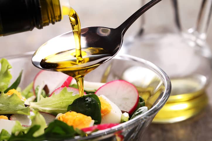 A tablespoon of MCT oil being poured over a salad