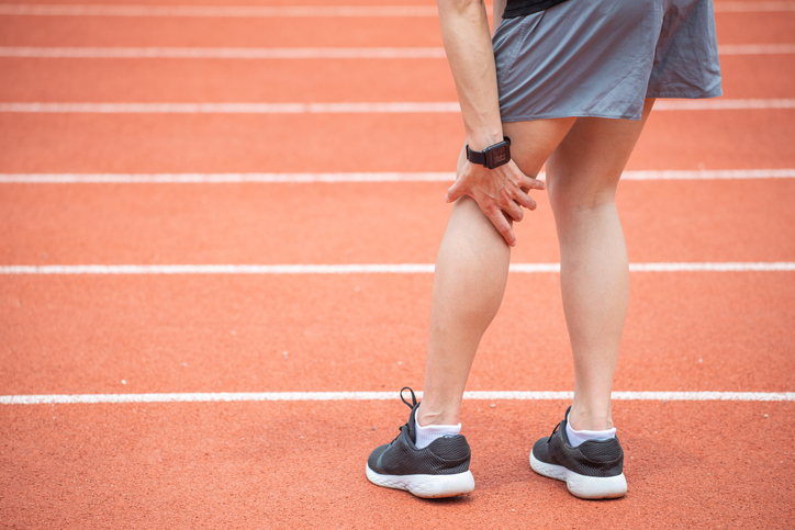 Woman on running track holding back of knee