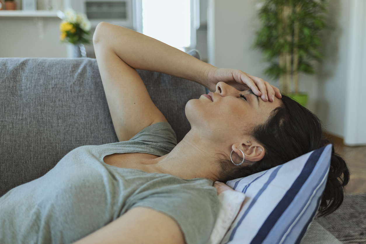Woman lying on sofa with headache and hand on forehead