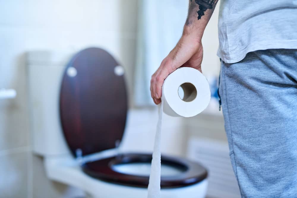 Person holding toilet roll facing toilet with symptoms of chronic idiopathic constipation