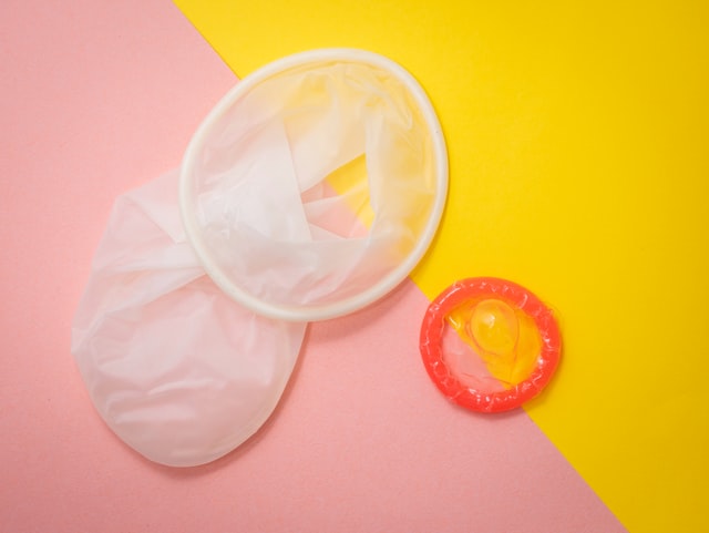 Male and female condom on pink and yellow background