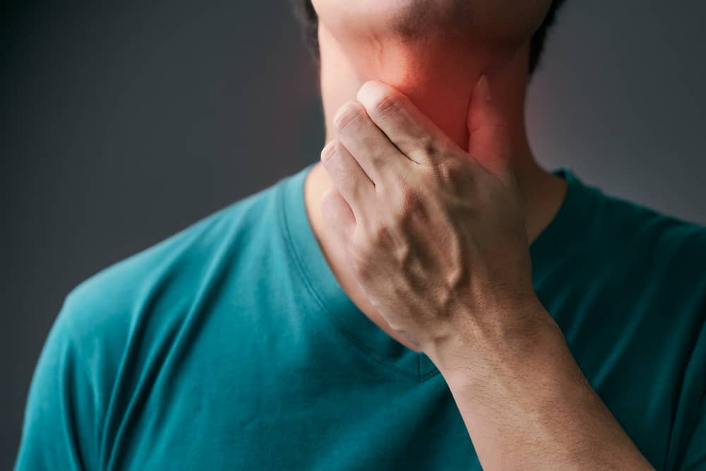 Person wearing green top holding throat with laryngeal larynx cancer