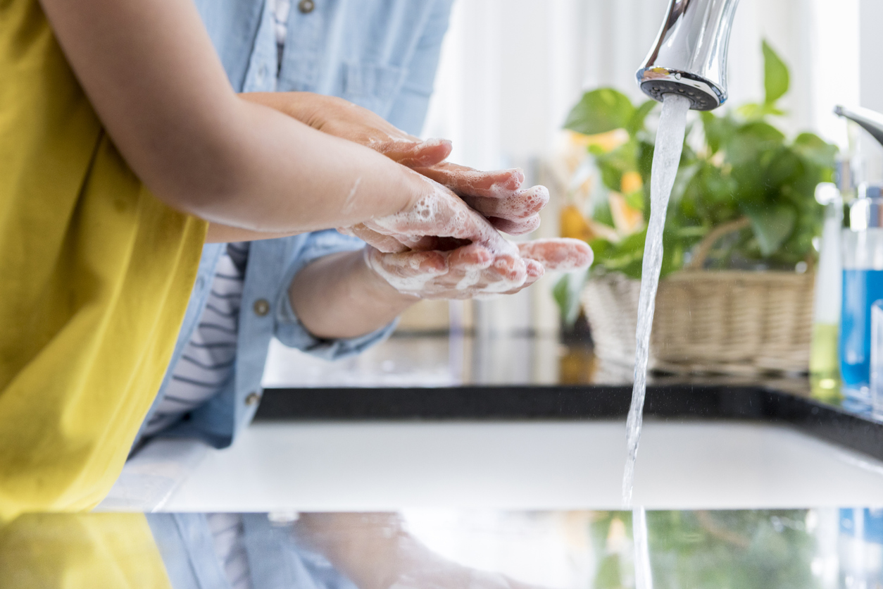 Parent and child stand at a kitchen sink washing hands with soap