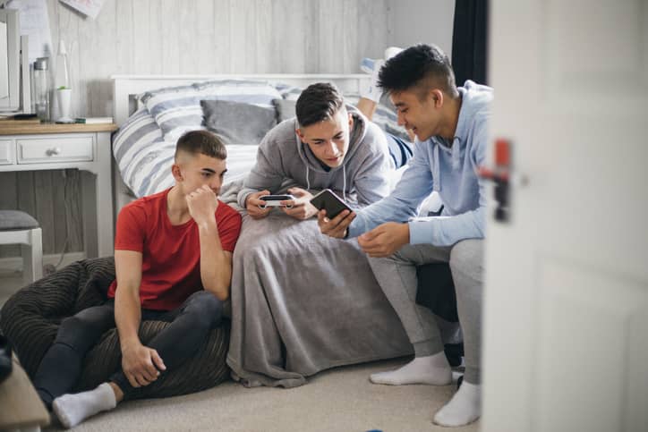 Three boys hanging out in bedroom looking at a phone