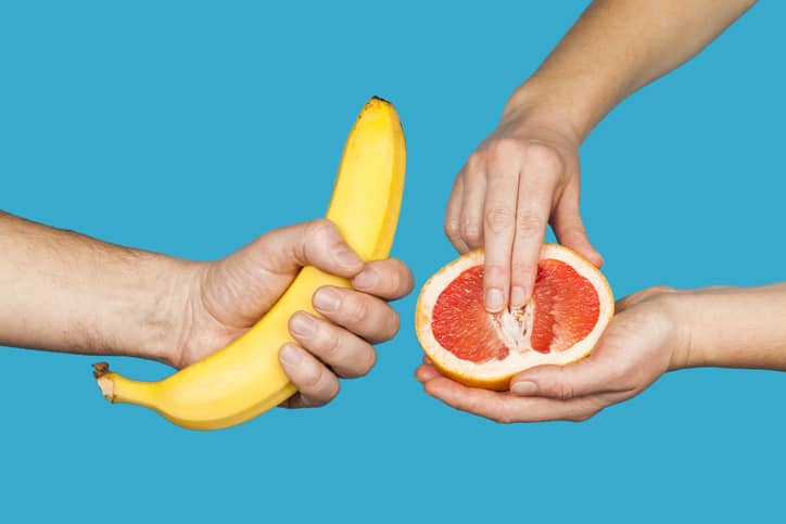 Banana and grapefruit in hands isolated on a blue background as a symbol of male and female masturbation. Games with the clitoris and touching the penis.