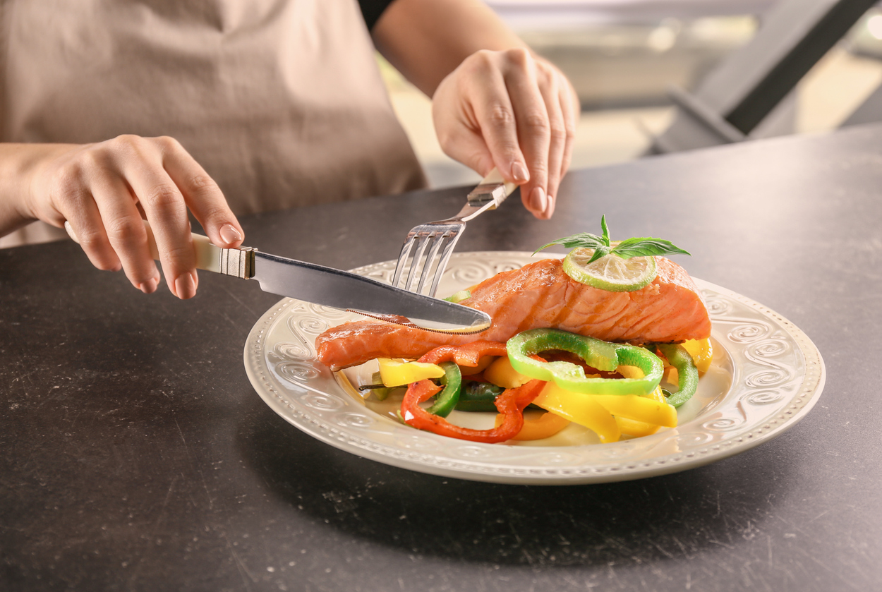 Woman eating salmon with fresh peppers at table (credit - serezniy)