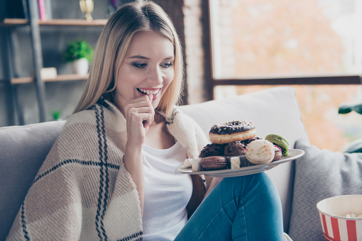 Woman sitting on sofa in living room, holding plate of donuts 