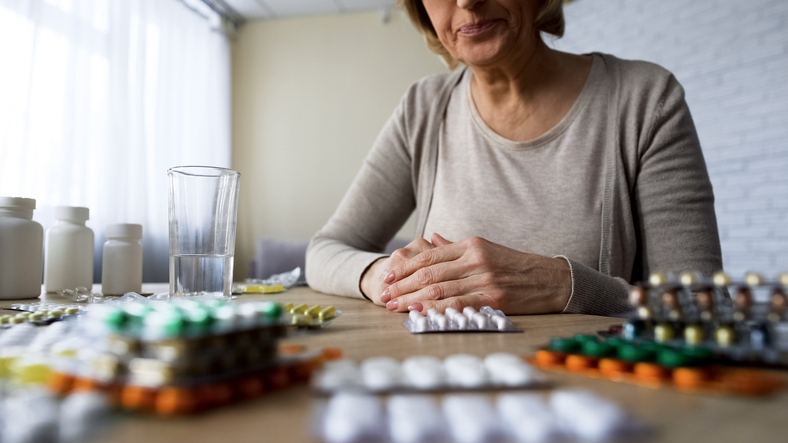 Older lady with pain looking at pills, painkillers 