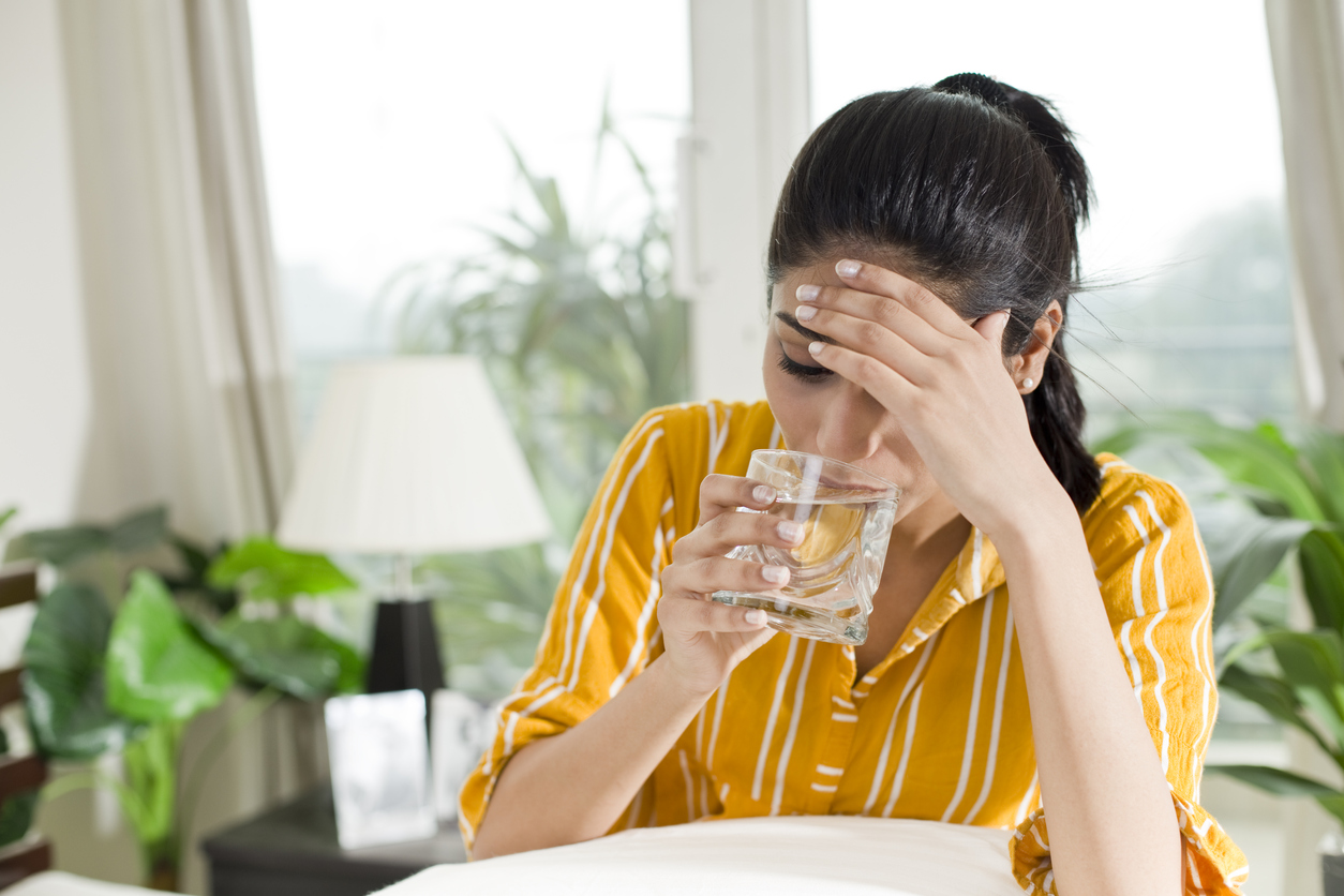 Woman with headache drinking a glass of water (credit - triloks)