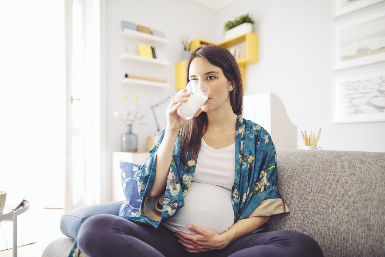 Pregnant woman sitting on couch drinking milk