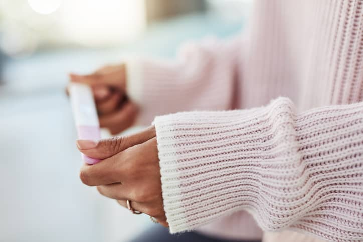 Person in a light pink knitted jumper holding a pregnancy test