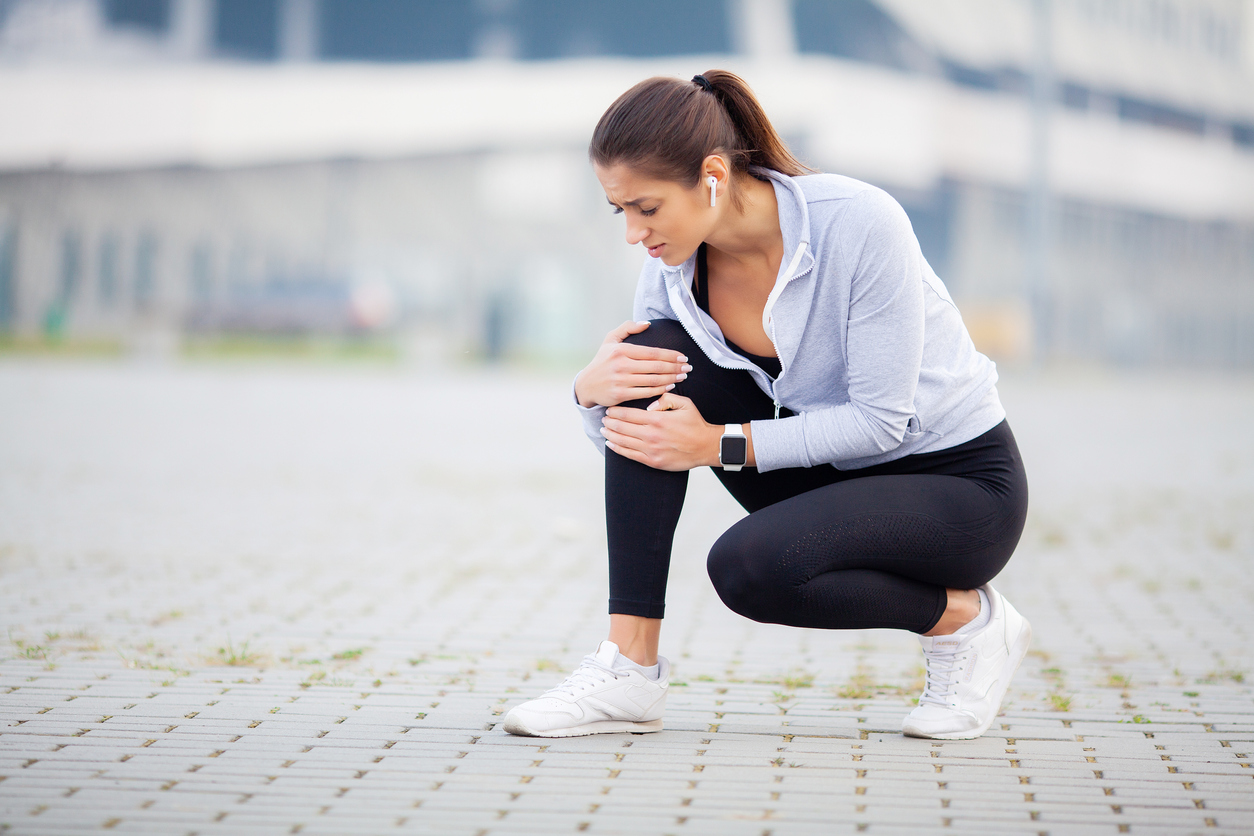  woman in running gear crouching and holding her knee in pain