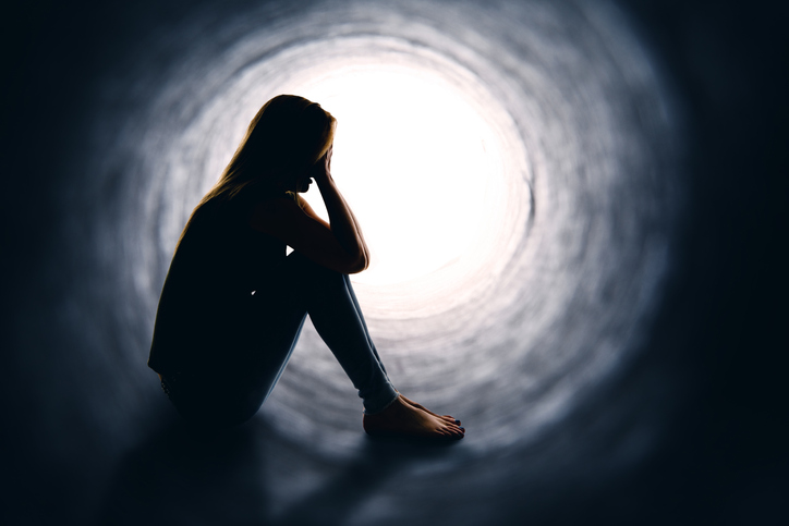 Depressed woman sitting alone is a dark tunnel with light at the other end