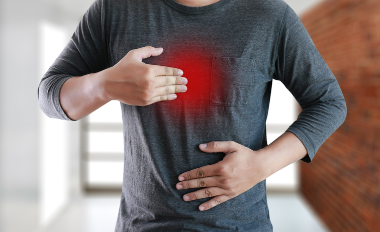 Man in grey t-shirt with hands on chest, with symptoms of heartburn