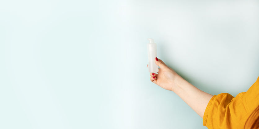 Person holding a transparent bottle of lube against a light blue background