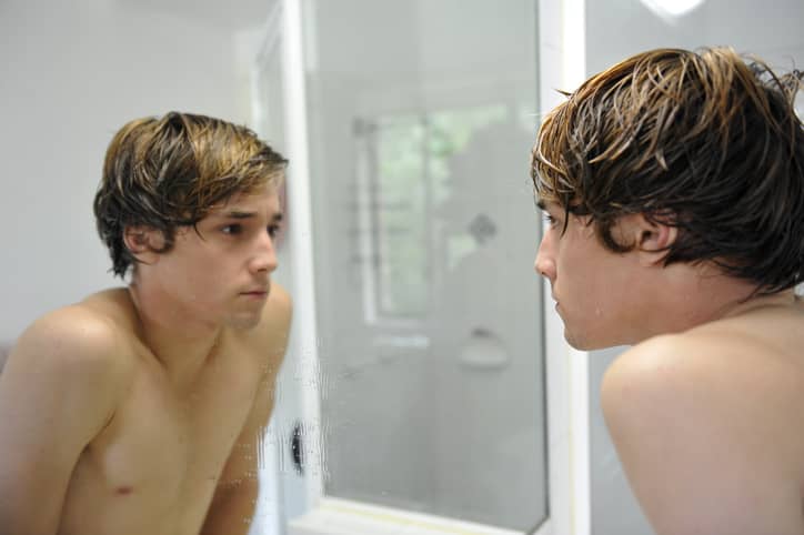 A teenage boy looking at his face in the bathroom mirror