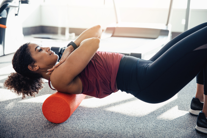 Young woman stretching her back at the gym, using a foam roller