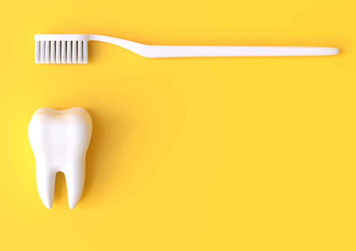 Flatlay image of a toothbrush and model tooth against a yellow background