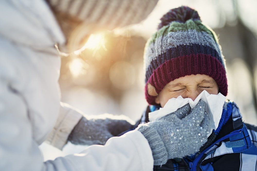 Mother blowing nose of her sick son during winter walk