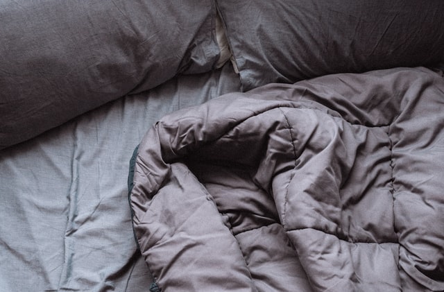 Messy unmade bed with grey-purple bedding