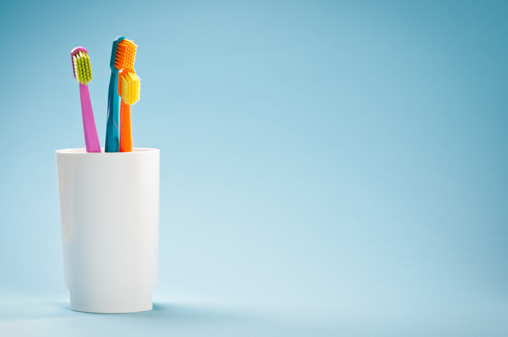 Orange, pink and blue toothbrushes in a white cup against a blue background