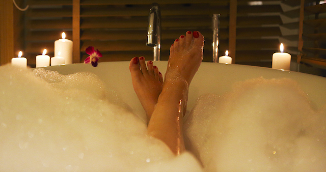 Woman-s feet coming out of bubble bath surrounded by candles warming feet before bed