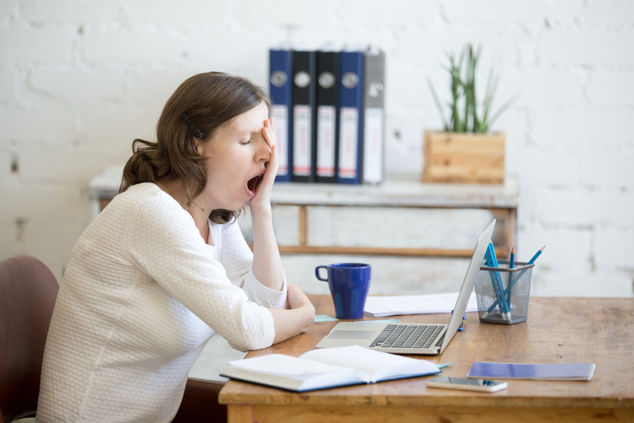 Young woman looking tired and yawning at her desk