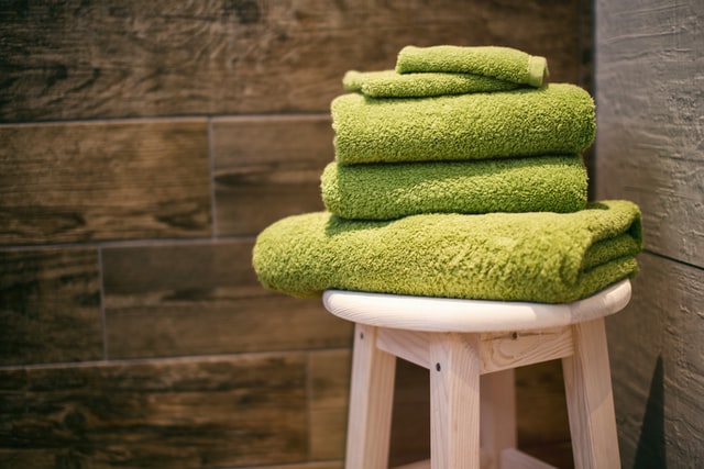 A bale of green towels on a wooden stool in a bathroom 