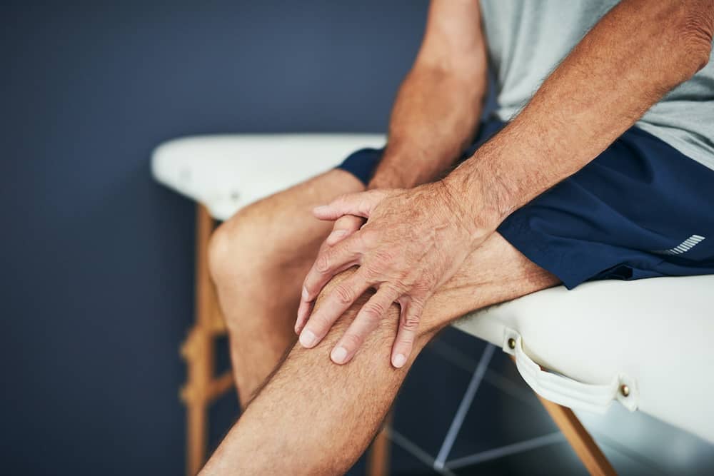 Person holding knee sitting on massage table with joint pain from cartilage damage