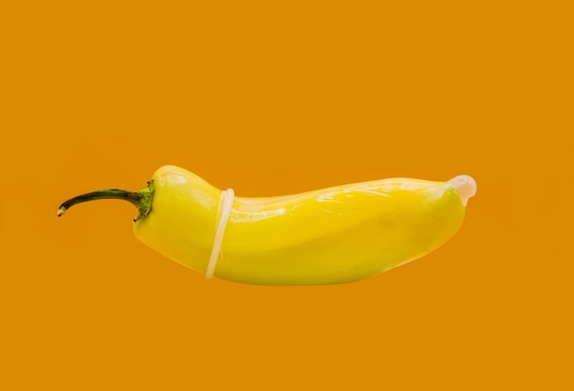 Yellow chilli with condom on orange background