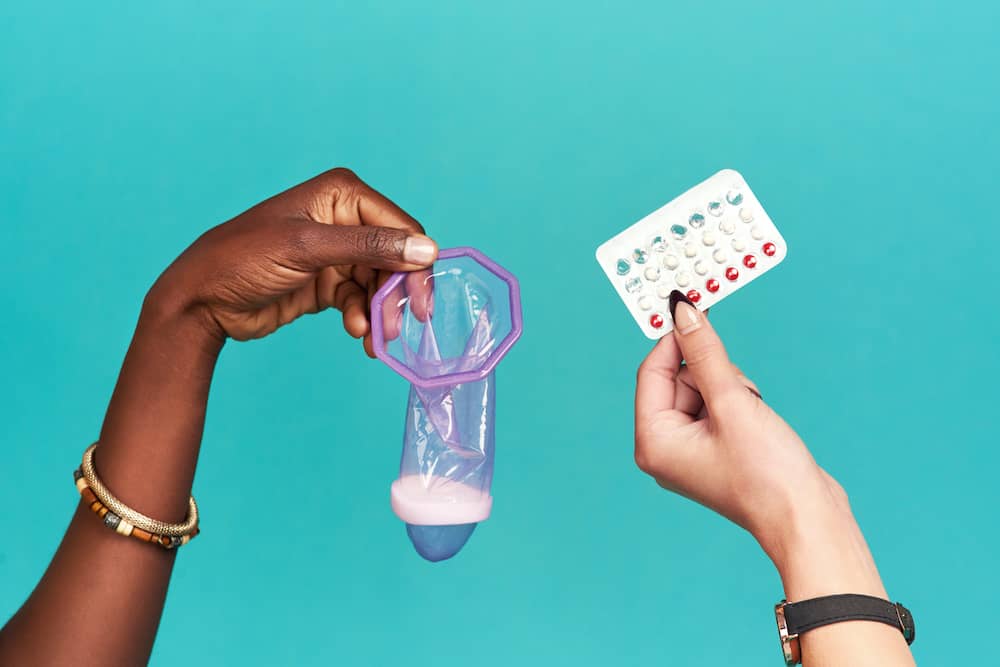 Hand holding female condom and hand holding contraceptive pill packet
