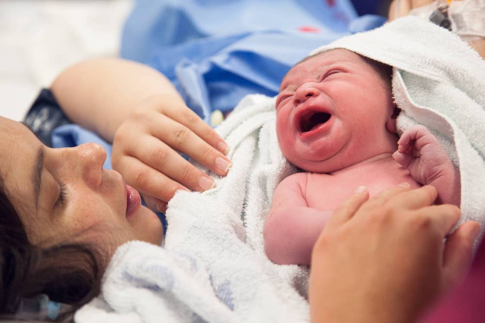 Mother in hospital gown holding new born baby after caesarean section