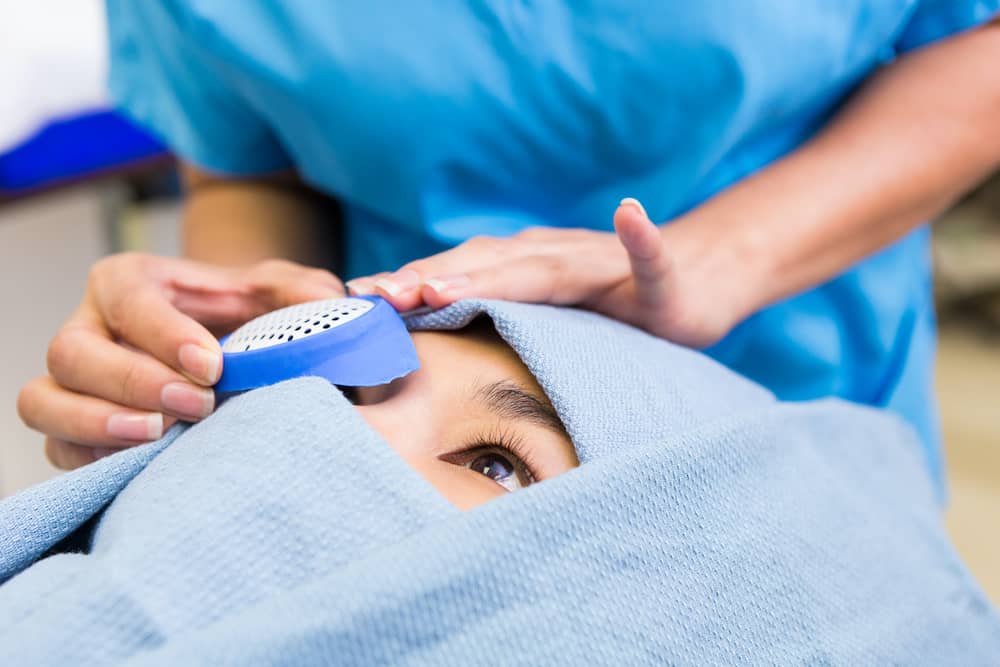 Person wrapped in blue surgical gown being prepared by nurse for cataract surgery