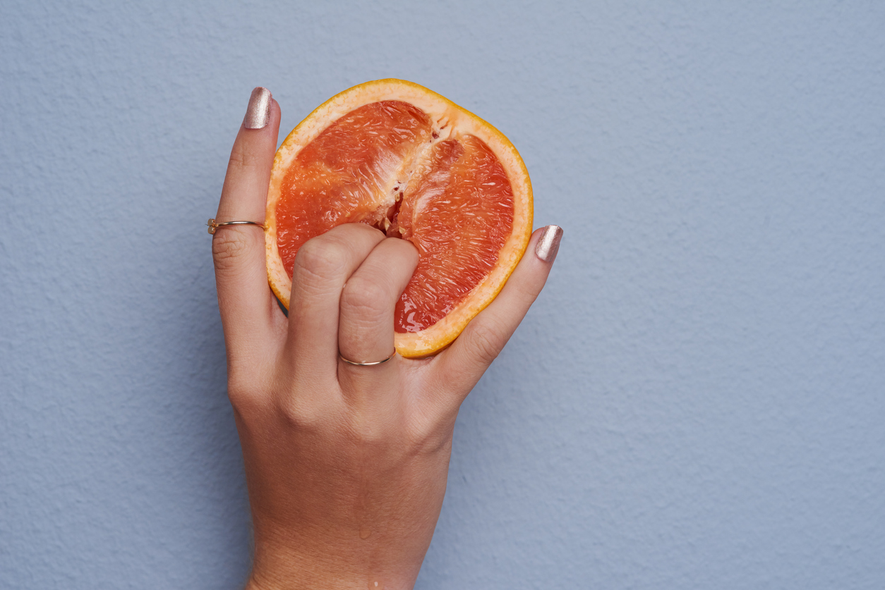 Cropped studio shot of an unrecognizable woman putting her fingers into a grapefruit against gray background