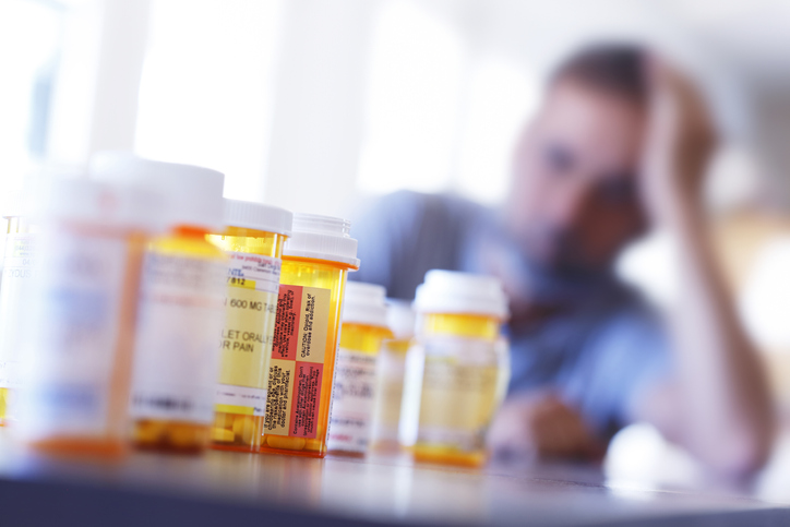 Group of prescription medication bottles sitting on a table in front of a man in the background