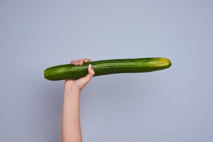Hand holding up a cucumber against a grey background