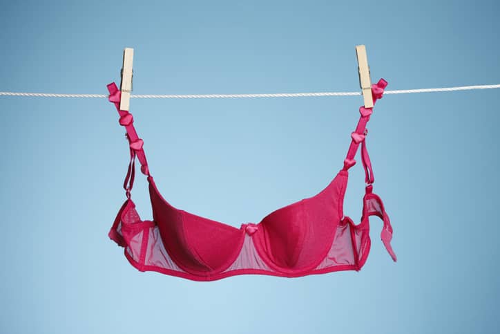 A hot pink bra hanging on a washing line with a blue background