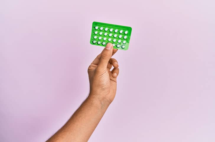 Hand holding male contraceptive pill in green packet on purple background