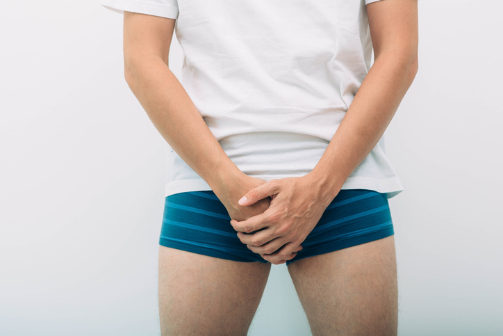 Man standing in underwear with hands over crotch
