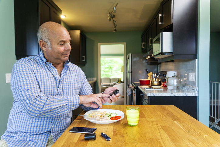 A diabetic patient in his kitchen testing his blood sugar prior to eating a healthy meal.