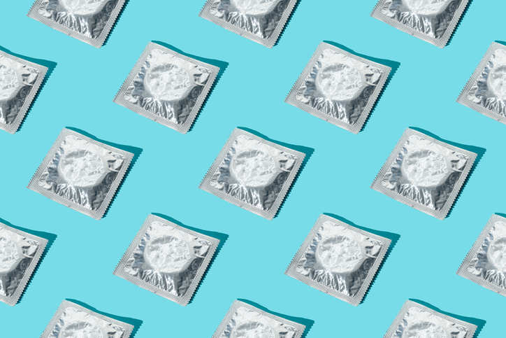 Multiple condoms in silver wrappers arranged in a geometric pattern against a bright blue background
