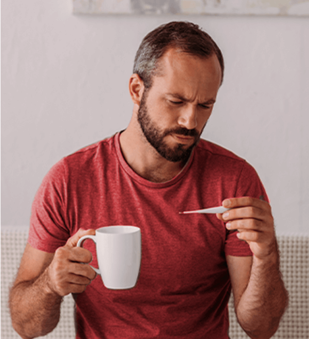 Hombre tomándose la temperatura con un café en la mano