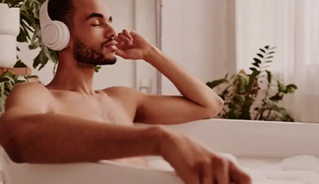 Hombre con auriculares tomando un baño de agua tibia en una bañera