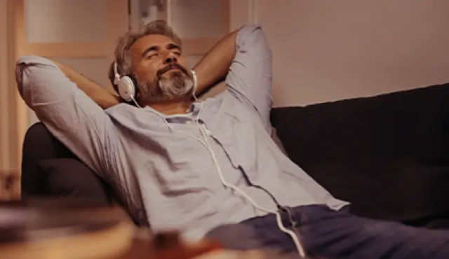 Hombre relajado escuchando música con auriculares blancos sentado en un sofá