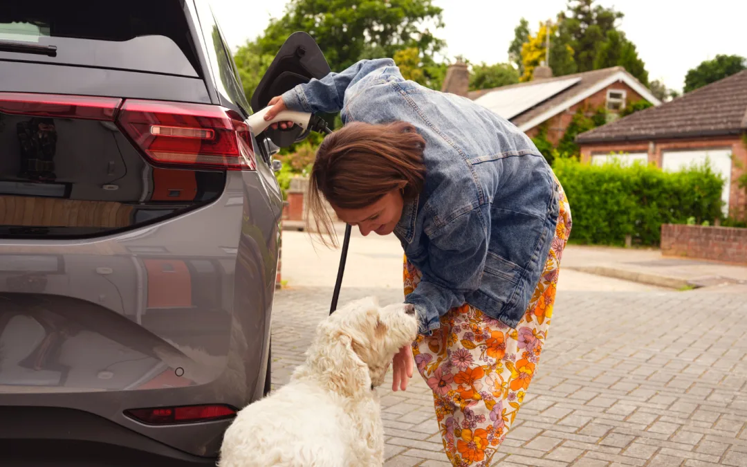 Woman charging her electric vehicles whilst stroking her dog