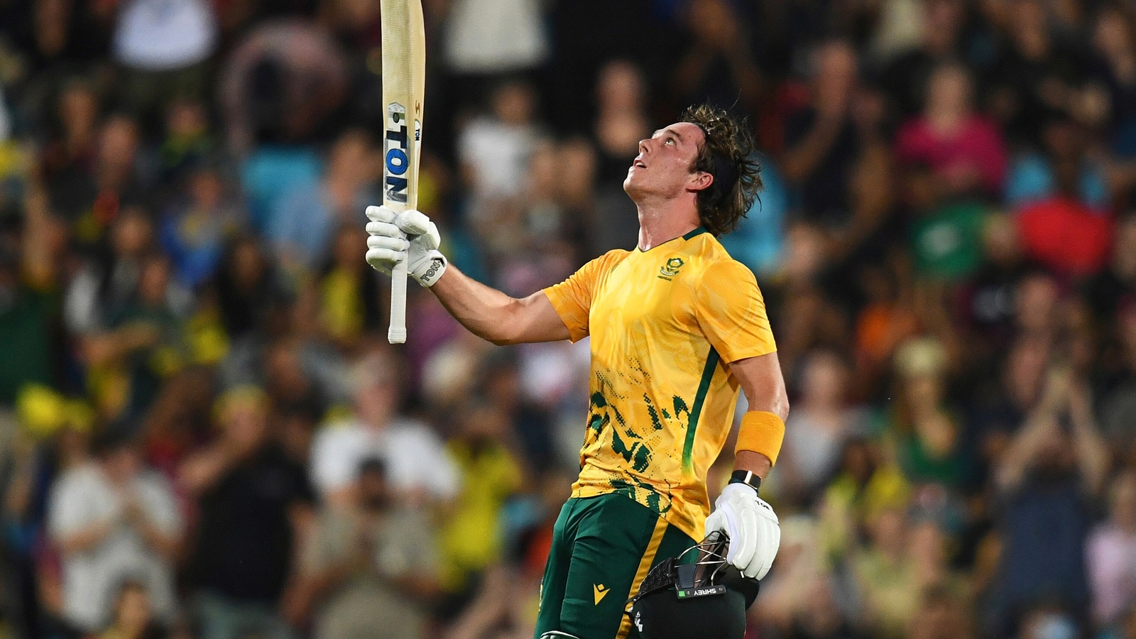 Dewald Brevis celebrating his maiden T20I century against Australia in 2025 holding his helmet and bat aloft.