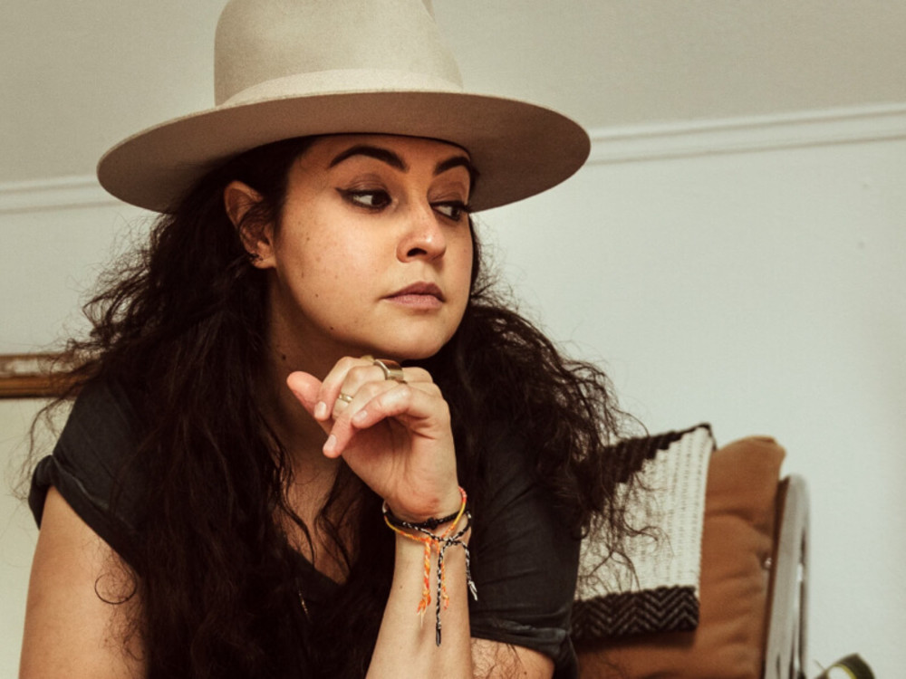 Femme aux cheveux foncés longs et au chapeau beige, l’air pensif, assise sur une chaise au stade de Toronto