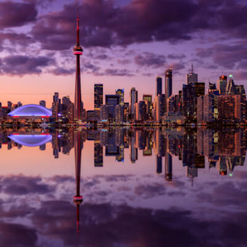 Toronto skyline at dusk, featuring the CN Tower and Rogers Centre, reflects on calm water
