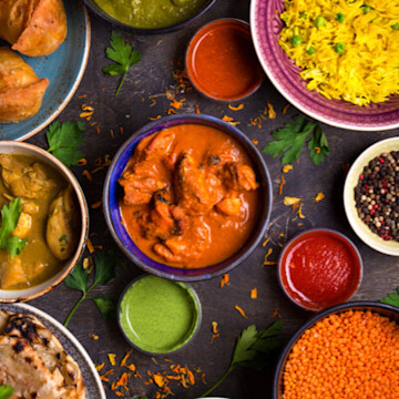 Close up of a vibrant spread of Indian cuisine with bowls of paneer, rice & butter chicken on a table